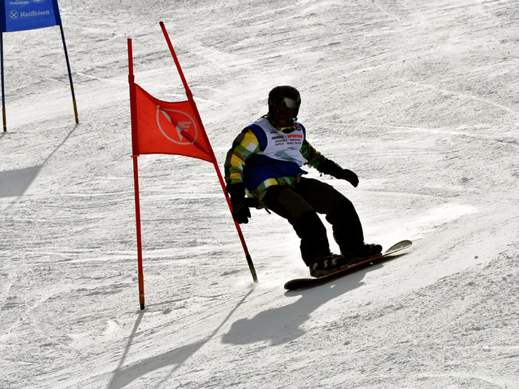 Snowboarder in tiefer Hocke umfährt ein rotes Tor.
